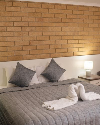 Comfortable grey bed with swan towels on top and brown couch