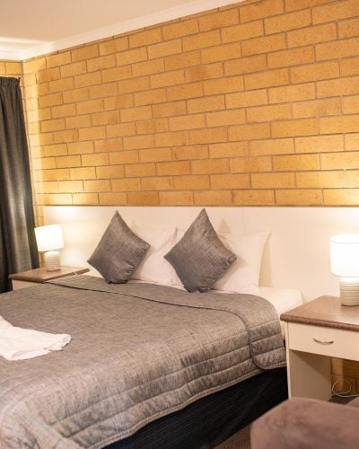 Brown couch, grey curtain, bedside table, table lamp and a comfortable bed
